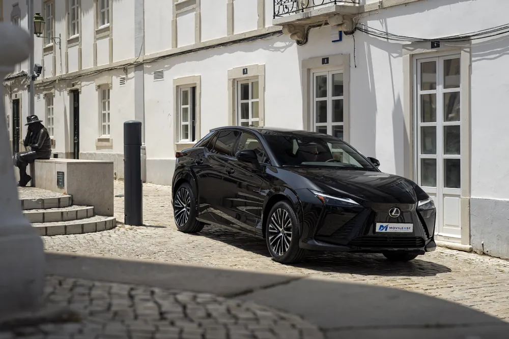 Lexus RZ e-Premium Efficiency, tres cuartos delantero en calle empedrada con fachadas blancas