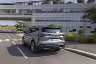 Renault Espace Techno E-Tech, tres cuartos trasero en marcha junto al mismo edificio