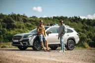 Subaru Outback Touring, tres cuartos delantero junto a la costa, con dos surfistas de kite