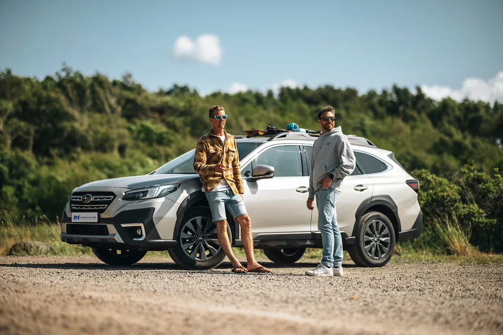 Subaru Outback Touring, tres cuartos delantero junto a la costa, con dos surfistas de kite
